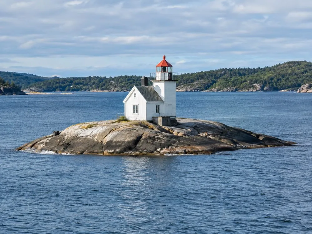 Der Leuchtturm Dyna allein auf seiner niedrigen, kahlen Schäre mitten im inneren Hafen: ein kleines weißes Gebäude auf einem Felsen knapp über dem Wasser, mit offenem Fjord auf allen Seiten.