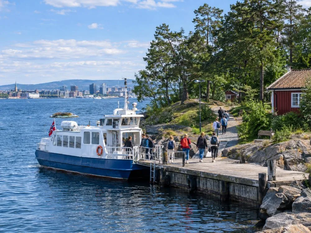 Ein Ruter-Inselfährboot an der kleinen Anlegestelle auf Hovedøya, während Passagiere an Land steigen auf der bewaldeten Insel, nur eine kurze Überfahrt vom Zentrum Oslos entfernt.